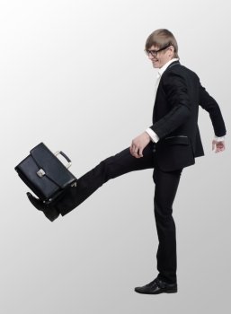 young businessman strikes foot for the briefcase on the white gray background

