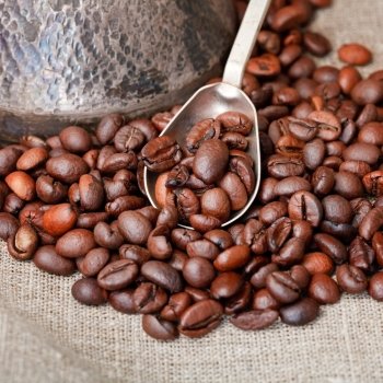 roasted coffee beans and copper coffee pot with spoon close up on textile