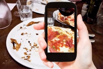 photographing food concept - tourist takes picture of italian pizza with parma ham and glass of red wine on smartphone, Italy