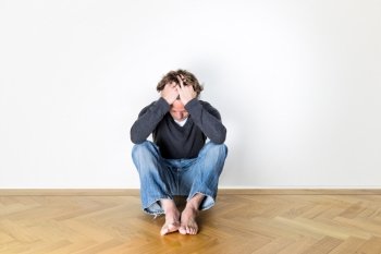 Young man, sitting depressed on a wooden floor.