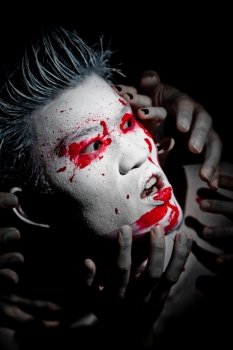 Young asian male closeup with red paint fashion makeup and white skin and hair on a black background with hands around his face