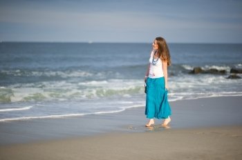 Young beautiful woman in white cami and turquoise skirt walks along the ocean