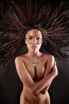 Portrait of a beautiful naked young african american woman with dreadlocks hair lying  
on a black background