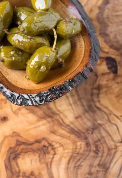 Green olives marinated with coriander in small wooden bowl over olive wood board, selective focus, copy space, top view