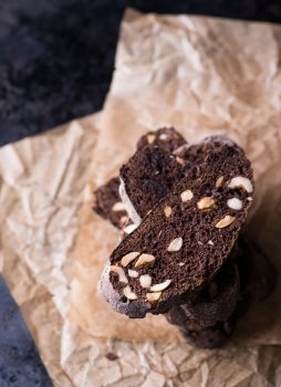 Dark chocolate biscotti with nuts on baking paper, top view, selective focus