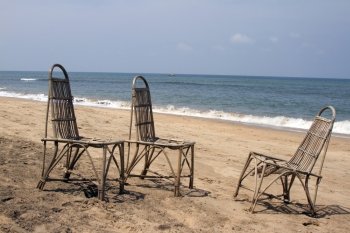Three wattled chairs stand on a beach, wait for people against the sea. GOA India beach.