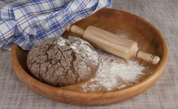 Fresh homemade bread made from durum wheat, rye, on a wooden tray with  a rolling pin. Composition on a beautiful tablecloths canvas. Photos for magazines about cooking, confectionery, cooking.