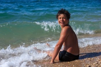 happy laughing boy of twelve sitting on the sea beach