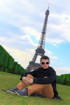 Young man hipster sits on the Champ de Mars near the Eiffel tower (La Tour Eiffel) in Paris, France