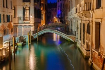 Lateral canal and pedestrian bridge in Venice at night with street light illuminating bridge and houses, Italy