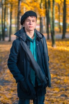 Serious teenage boy in a cap, scarf and jacket in the autumn sunny park. Toning in warm tones