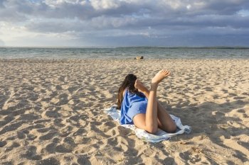 Rear view of pretty girl lying on sandy beach on hot summer 