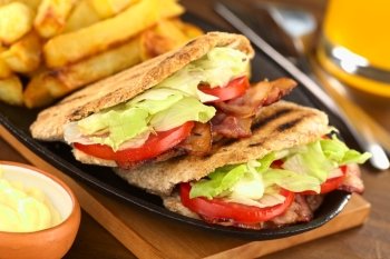 BLT (bacon, lettuce, tomato) wholewheat pita sandwich with French fries and mayonnaise in the front (Selective Focus, Focus on the front of the two pita stuffings)