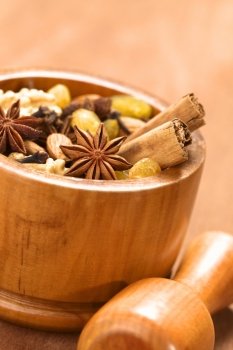Baking ingredients such as star anise, clove, cinnamon, almond, raisin, sultana and walnut in wooden mortar with pestle in front (Selective Focus, Focus on the middle of the star anise in the front) . Baking Ingredients in Mortar