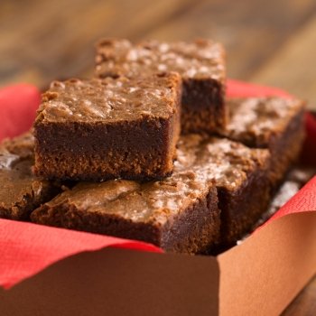 Freshly baked brownies in a brown paper box with red napkin (Selective Focus, Focus on the first brownie on the top)