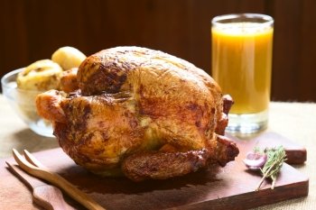 Roast chicken on wooden board with potatoes and juice in back, photographed with natural light (Selective Focus, Focus on the front of the chicken)