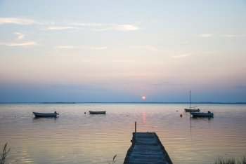 An old wooden jetty with anchored small boats in a calm bay at twilight time