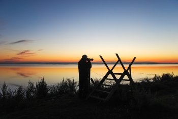 Silhouette of a photographer by a stile at the coast at twilight time