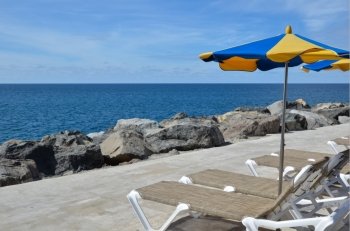 Sunbeds and colorful parasol by a coast with clear blue water