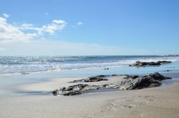 Glittering water and blue sky at a beach with sand and flat rocks
