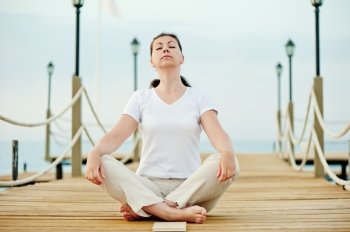 beautiful girl sitting in the lotus position on a pier with his eyes closed