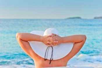 woman takes a sunbath in white hat near the sea