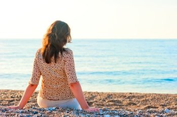 woman admiring the sea while sitting on a pebble beach