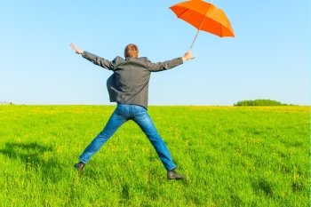 businessman with umbrella jumping in a field