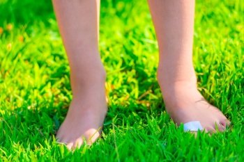 barefooted child with a plaster on a foot stands on lush grass