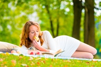 Red-haired student eats an apple and reading books in the park