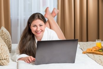 beautiful girl after the shower lying on the bed with laptop