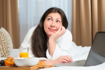 smiling dreamy girl with laptop and breakfast