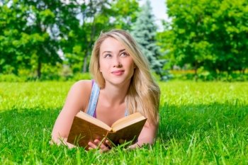 pretty blonde lying on the grass and holds in hands thick book