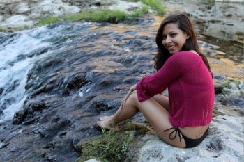 Hispanic woman sitting at water edge of a creek.