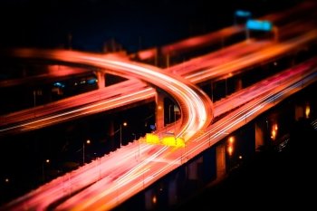 Tilt shift blur effect. Abstract cityscape background. Futuristic night aerial view of highway interchange with moving cars. Bangkok, Thailand