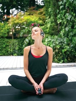 Beautiful young woman in earphones doing yoga exercise outdoors 