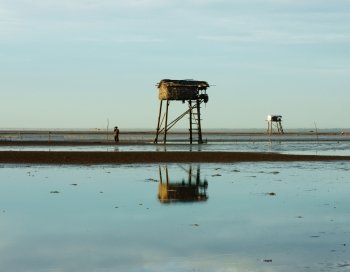 Wooden watch tower on Viet Nam beach at Mekong Delta,watchtower reflect on water, sea with black sand, people standing on sand