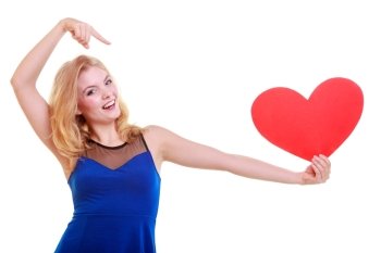 Red heart card. Love symbol. Beautiful woman hold Valentine day symbol pointing. Cute blonde girl in blue dress expressing tender feelings. Isolated studio shot