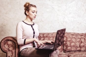 Technology internet modern lifestyle concept. Young business woman or student girl using laptop working on computer sitting on retro couch. Indoor. Vintage photo.