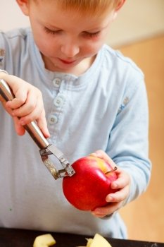Blond boy child kid preschooler peelings fruit apple at home. Happy childhood.