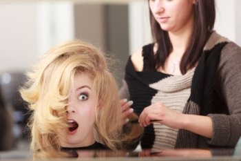 Surprised shocked girl with blond wavy hair by hairdresser. Hairstylist combing female client. Young woman in hairdressing beauty salon. Hairstyle.