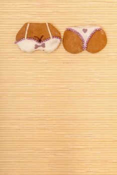 Funny bikini underwear shape gingerbread cake cookie sweet dessert with yellow icing and pink decoration border or frame on beige bamboo mat background