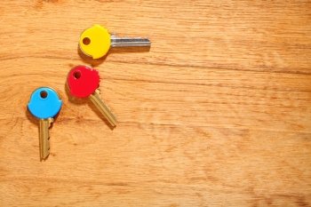 Three house keys with colorful plastic coats caps on wooden table background. Copy space for text