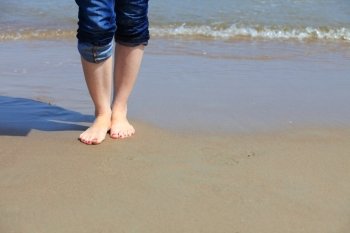 Female legs walking in water, girl's barefoot legs on the sand beach
