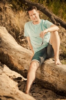 Happiness summer vacation and people concept. Fashion portrait of handsome man on the beach, guy sitting on tree by sea landscape