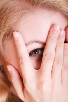 Closeup of afraid frightened woman peeking through her fingers. Shy girl covering face with hands.