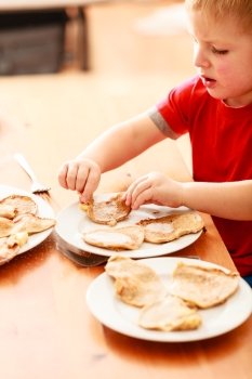 Little boy eating fried apple in pancake dough or apple fritters pancakes with icing sugar at home
