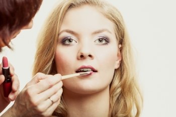 Cosmetic beauty procedures and makeover concept. Makeup artist applying lipstick with accessories tools to woman lips.