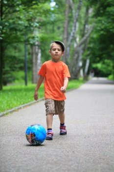 Boy young kid playing with ball kicks running towards ball in park outdoors