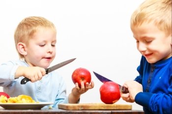 Children little boys brothers playing dangerous game with kitchen knife cutting apple, making salad at home.